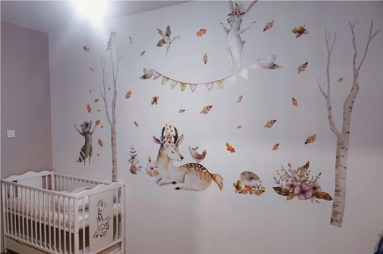Pokój dziecięcy z białym łóżeczkiem i naklejkami ściennymi przedstawiającymi leśne zwierzęta, drzewa i liście w stylu akwareli.