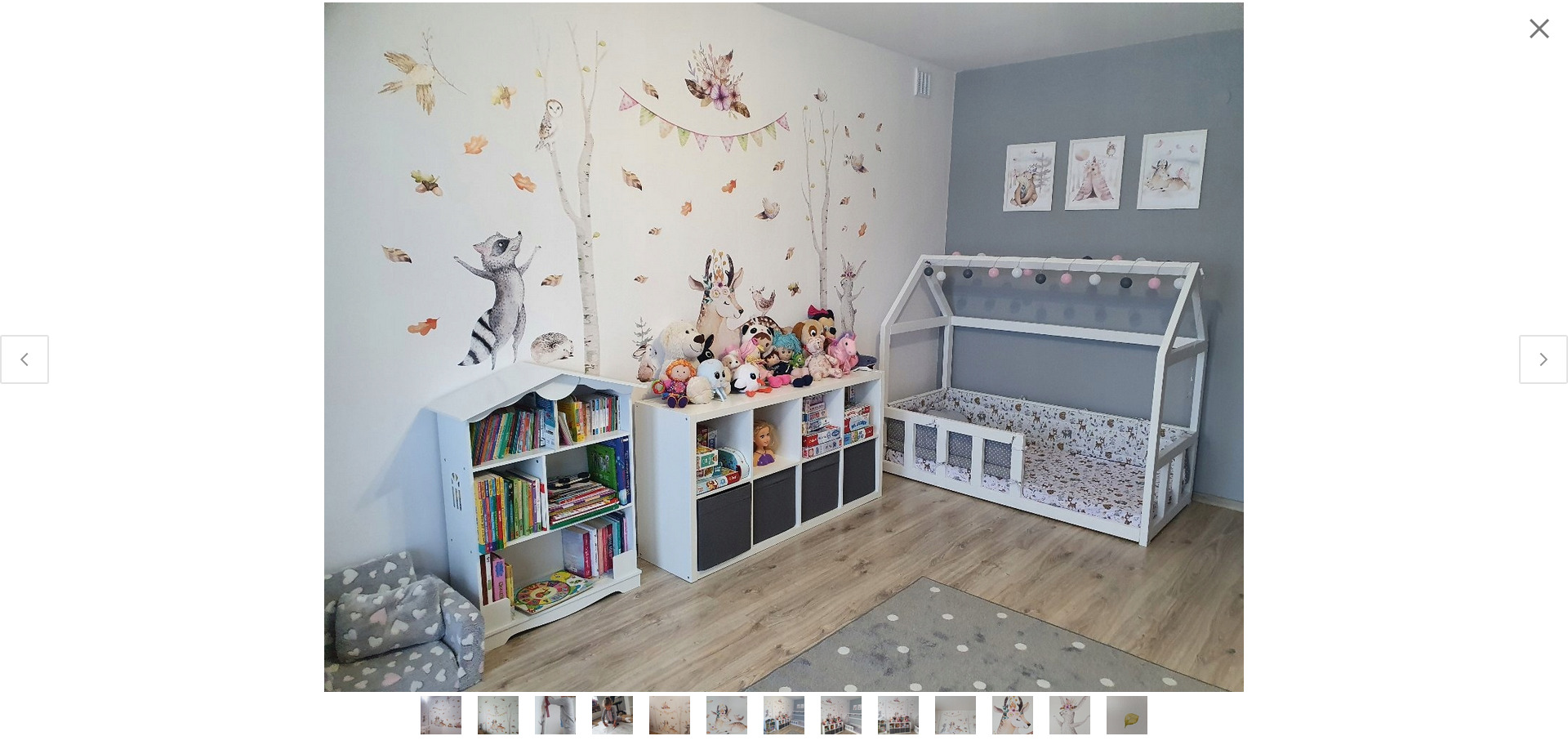 Pokój dziecięcy z łóżkiem w kształcie domku, białym regałem na książki w kształcie domku, komodą z szufladami i szarą ścianą z naklejkami zwierząt w stylu leśnym.