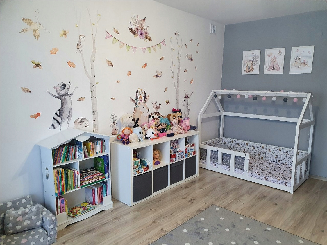 Pokój dziecięcy w stylu skandynawskim z białymi meblami, łóżkiem w kształcie domku, regałem na książki i naklejkami ściennymi z motywami zwierzęcymi.