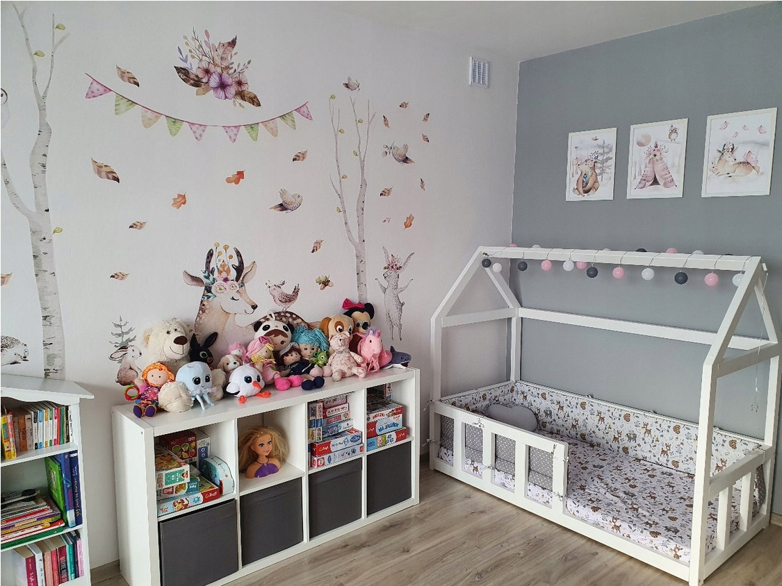 Pokój dziecięcy w stylu skandynawskim z łóżkiem w kształcie domku, regałem na zabawki i naklejkami ściennymi z motywem zwierząt leśnych.