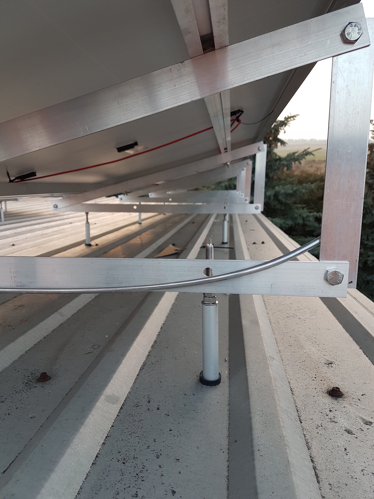 Szczegółowe ujęcie montażu paneli słonecznych na dachu z blachy trapezowej, widoczne aluminiowe profile montażowe, regulowane wsporniki i elementy mocujące.