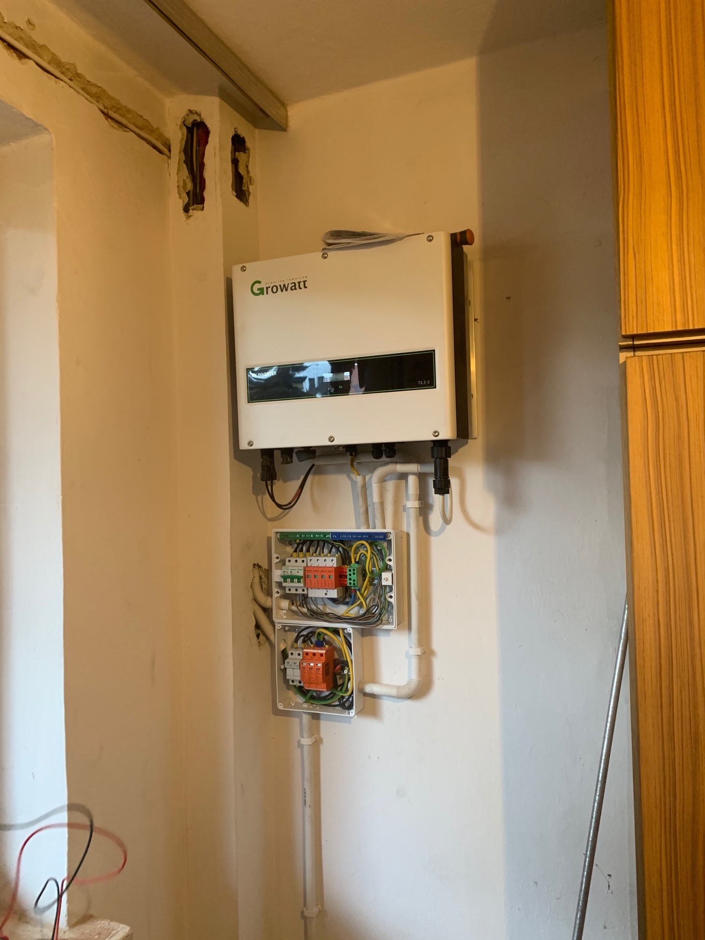 Zamontowany inwerter marki Growatt TL3-S oraz dwie otwarte puszki elektryczne z widocznymi przewodami i zabezpieczeniami, umieszczone na ścianie w trakcie instalacji.