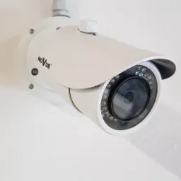 Kamera IP marki Novus zamontowana na białej, lekko chropowatej ścianie, widoczny cień kamery.