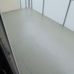 Firma Budowlana Przemysław Żurko - Balkon po wylaniu samopoziomującej wylewki, widoczne mokre podłoże i szara balustrada z białym wypełnieniem, w tle las.