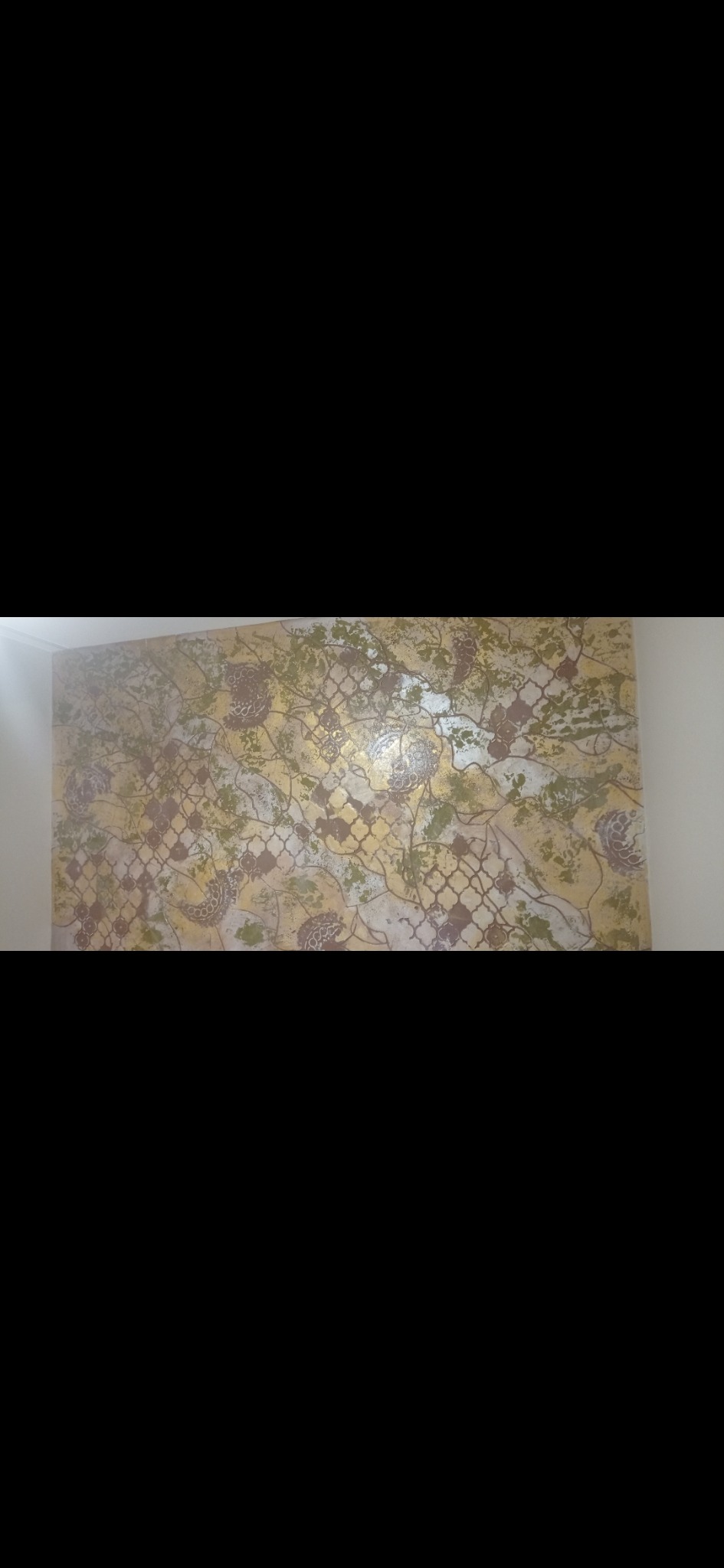 Dekoracyjna ściana z efektem szlachetnej patyny, wzór w stylu marokańskim z motywami roślinnymi w odcieniach złota, brązu i zieleni, oświetlona z lewej strony.