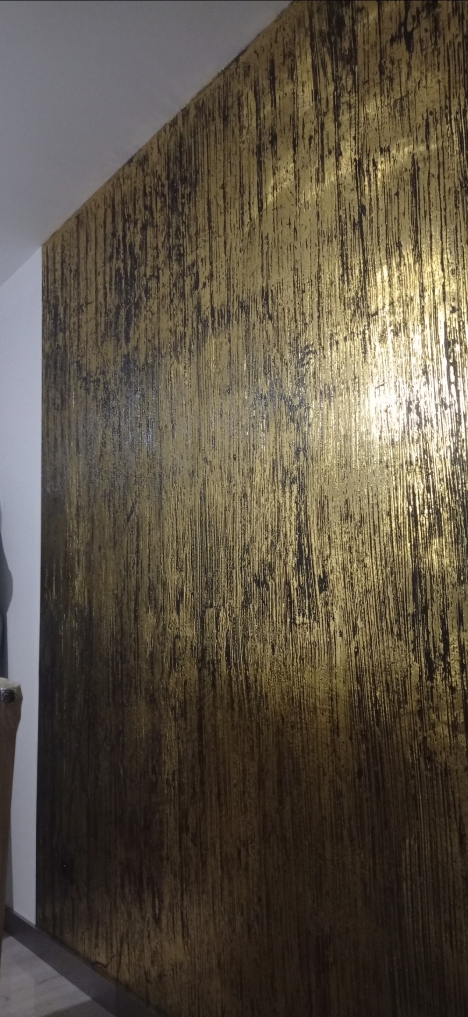 Ściana z dekoracyjną, pionową fakturą w odcieniach złota i brązu, wpadająca w światło.