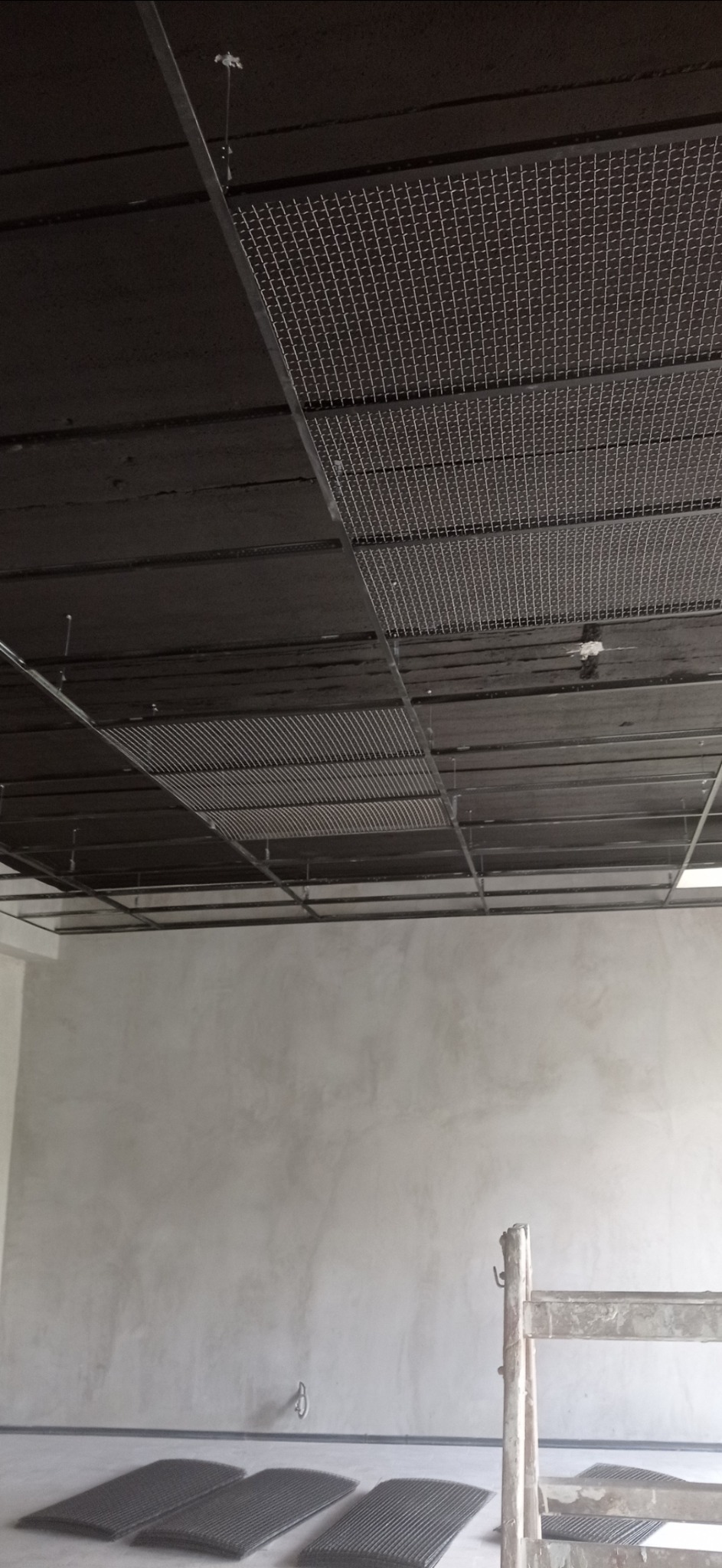 Montaż sufitu podwieszanego z widoczną konstrukcją metalową i elementami siatki, ściany w trakcie wykończenia, drabina w tle.