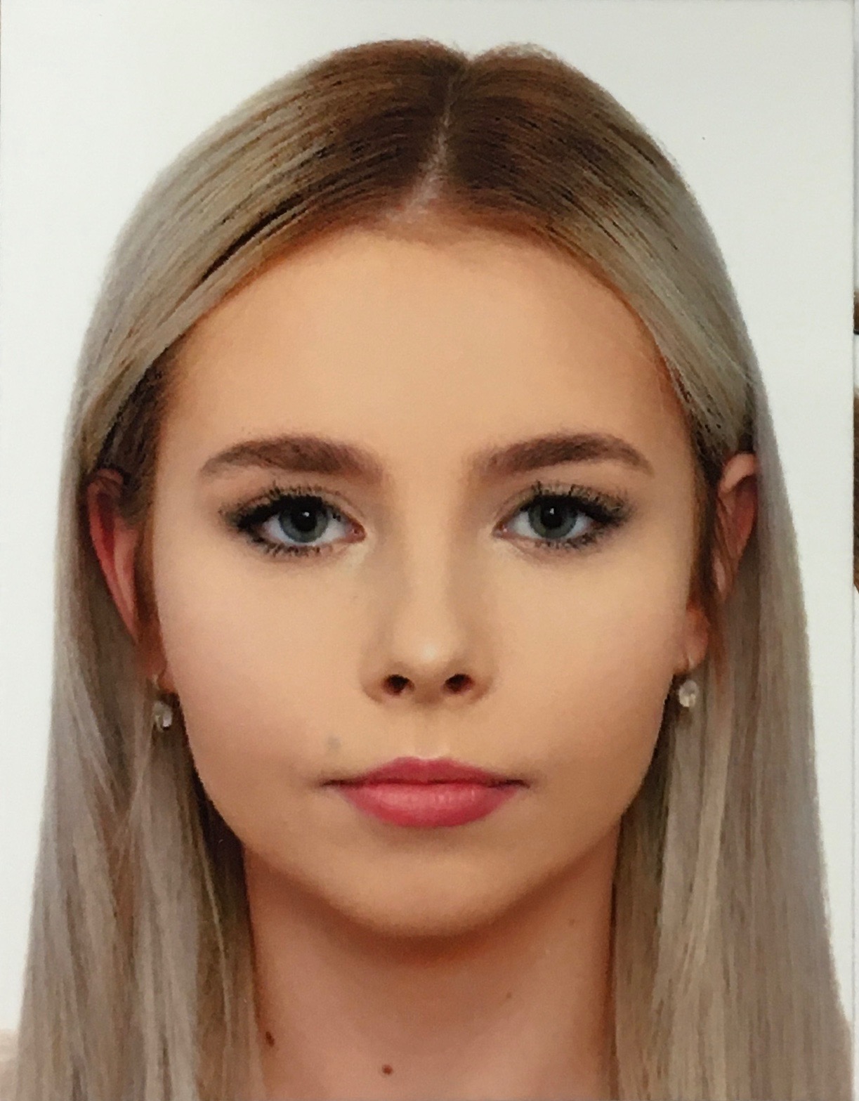 Portret młodej kobiety z blond włosami i niebieskimi oczami, na białym tle. Widoczne delikatne kolczyki.