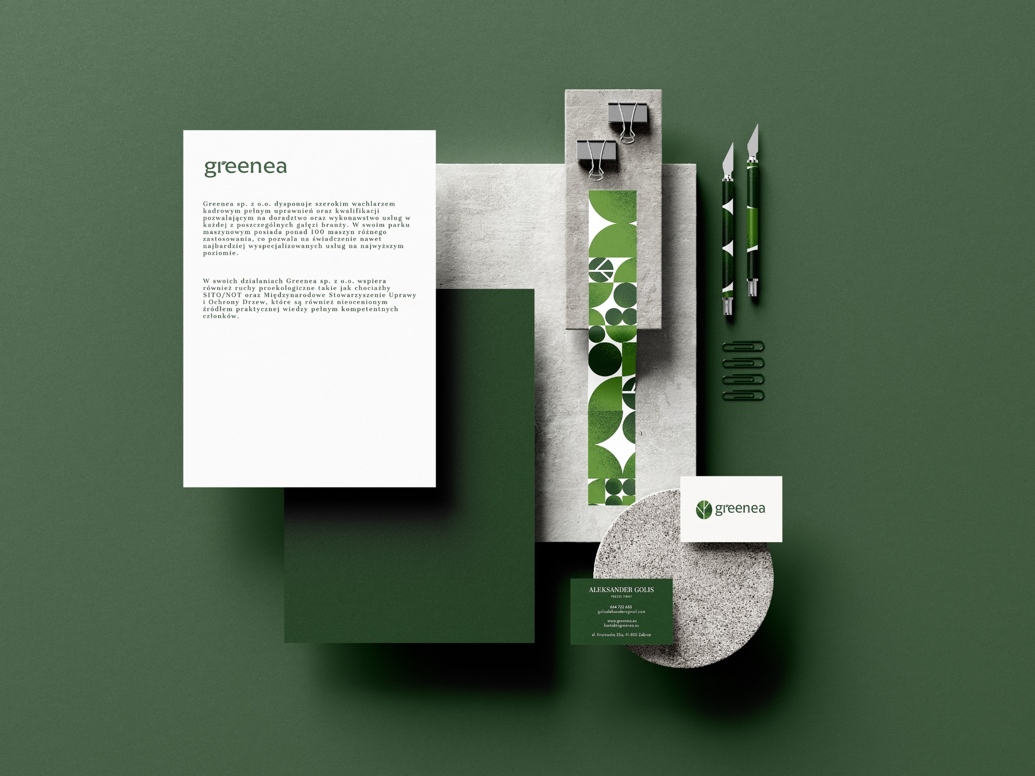 Zestaw materiałów firmowych w odcieniach zieleni, prezentujący logo, wizytówki, papier firmowy i narzędzia biurowe na ciemnozielonym tle, tworzący minimalistyczną kompozycję.
