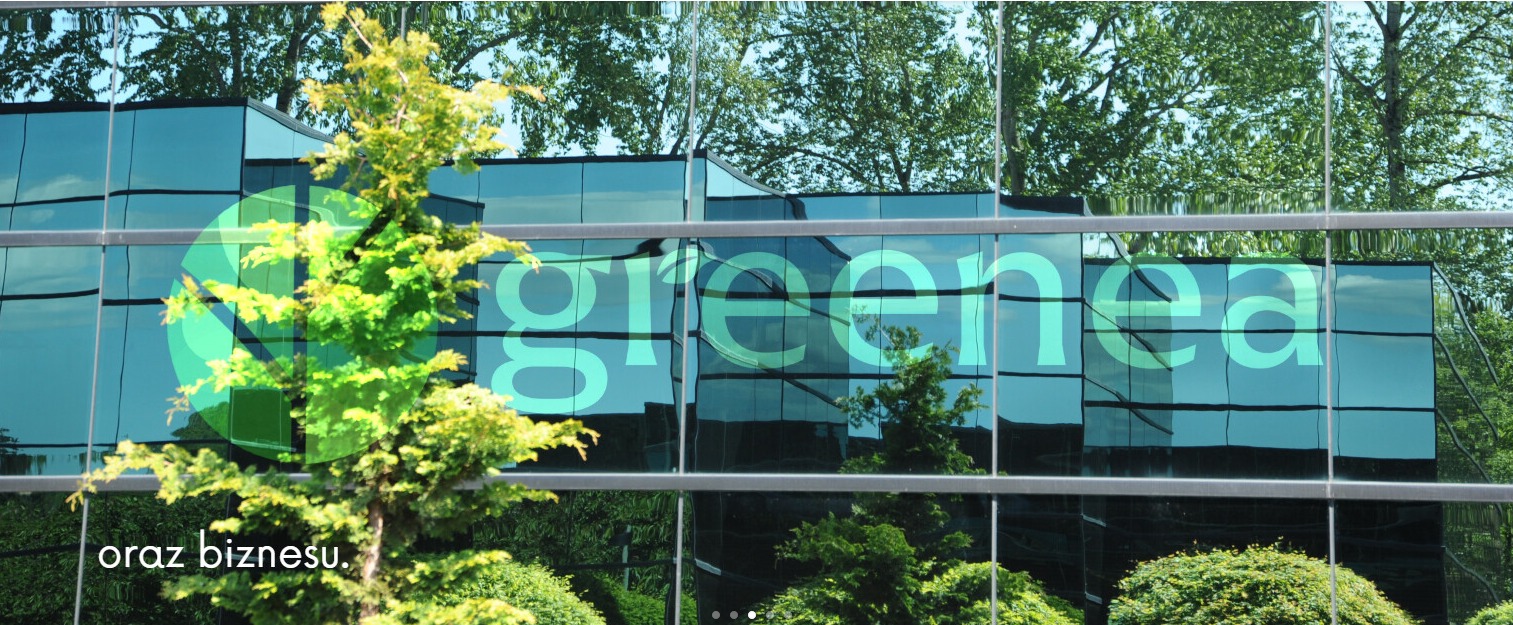 Logo firmy ogrodniczej 'greenea' umieszczone na szklanej fasadzie biurowca, z widocznymi krzewami i drzewami w otoczeniu.