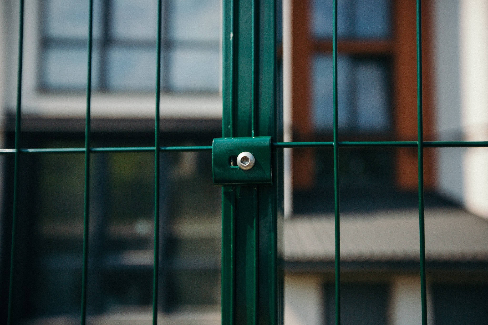 Fragment zielonego ogrodzenia panelowego z widocznym mocowaniem na tle budynku.