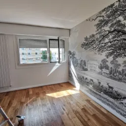 Pokój po tapetowaniu z fototapetą w stylu retro przedstawiającą krajobraz z jeleniami, parkiet drewniany, drabina malarska w rogu.