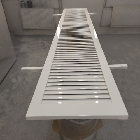 Świeżo polakierowane na biało drewniane drzwi lamelowe, leżące poziomo na stojakach w pomieszczeniu warsztatowym.