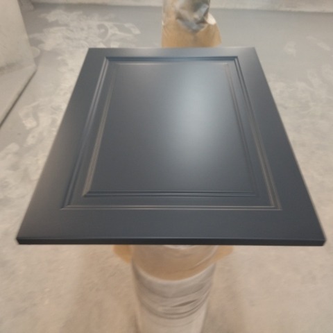 Pomalowane na szaro, frezowane drzwiczki szafki kuchennej, ustawione na statywie w pomieszczeniu lakierniczym.