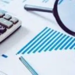 Kalkulator, lupa i okulary na tle wykresu z niebieskimi liniami, sugerujące analizę finansową.