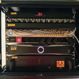 Szafa Rack z panelem chłodzącym, patch panelem, organizerem kablowym, switchem PoE, listwą zasilającą, rejestratorem CCTV i UPS, zamontowana wewnątrz obudowy.