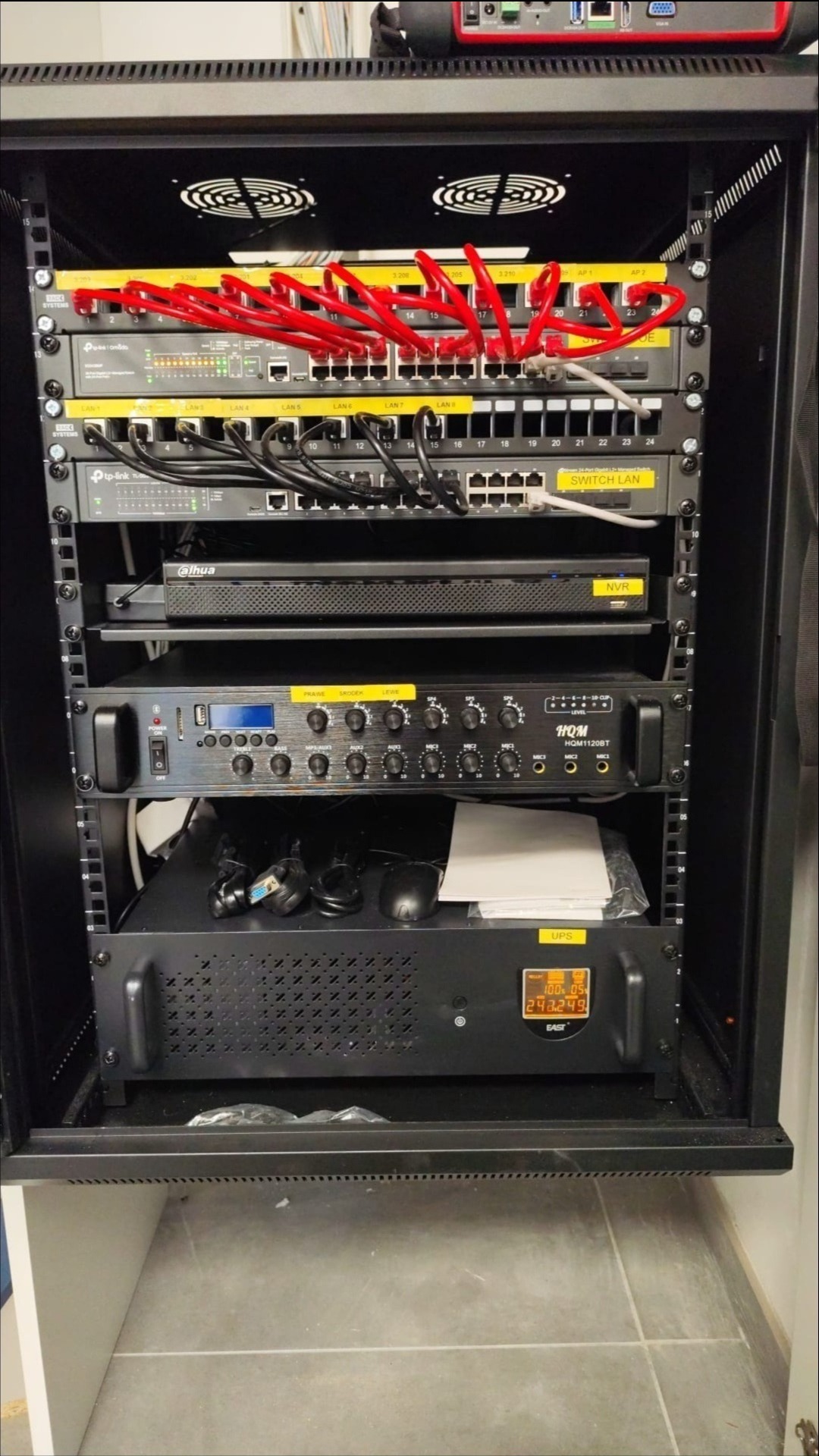 Szafa Rack z patch panelami, switchami, rejestratorem IP CCTV, wzmacniaczem dźwięku i UPS. Kable sieciowe wpięte, etykiety na urządzeniach. Rozwiązanie sieciowe i zasilania awaryjnego.