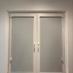 Dwuokienne okno z zamontowanymi szarymi roletami wewnętrznymi, widoczne mechanizmy sterujące i marmurowy parapet.