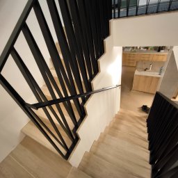 Vaanto - Nowoczesne schody z czarną balustradą w Zielątkowie. Ujęcie z góry podkreśla oryginalny design i eleganckie wykończenie. Widoczne drewniane stopnie i minimalistyczny styl.