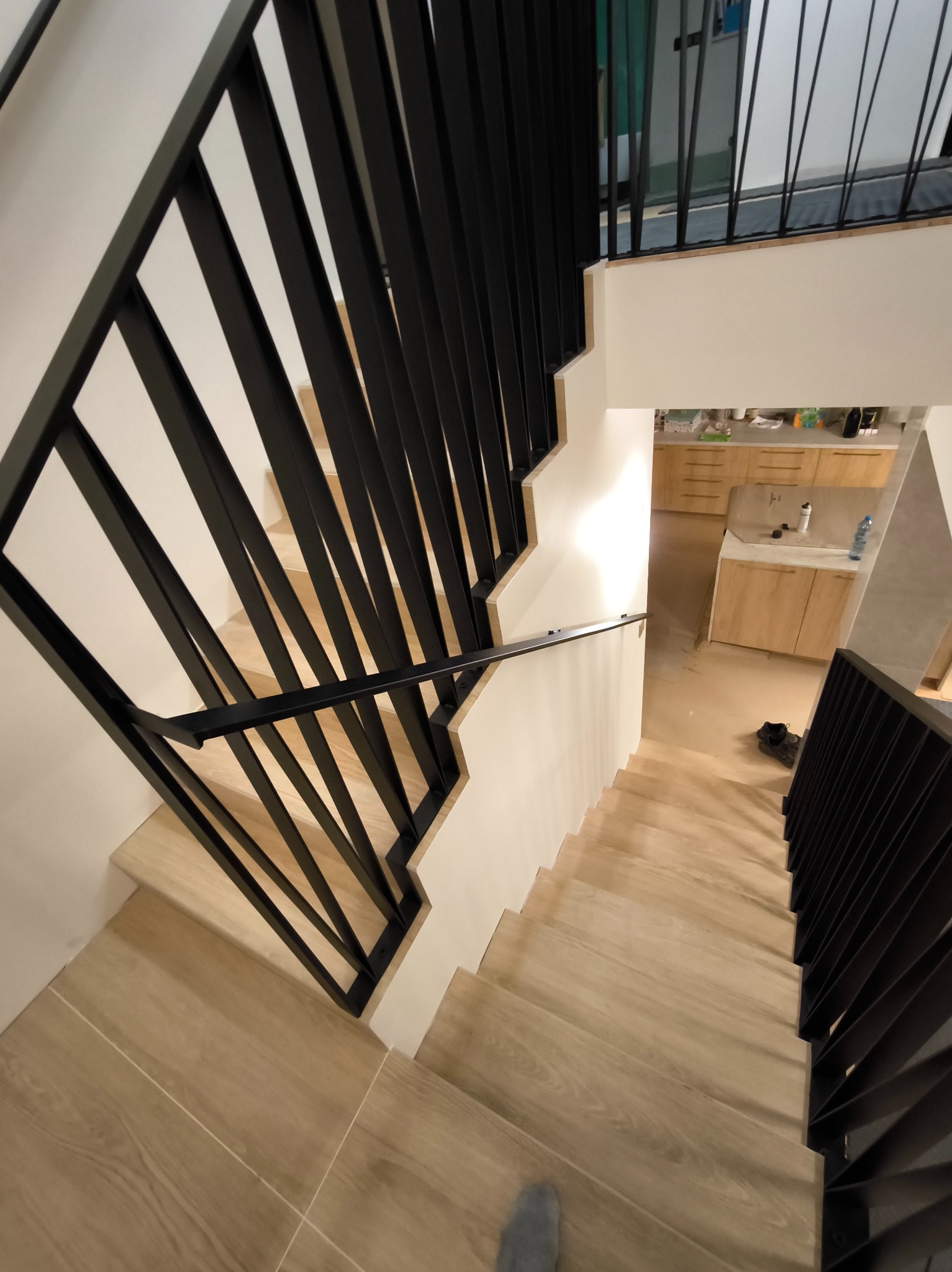 Nowoczesne schody z czarną balustradą w Zielątkowie. Ujęcie z góry podkreśla oryginalny design i eleganckie wykończenie. Widoczne drewniane stopnie i minimalistyczny styl.