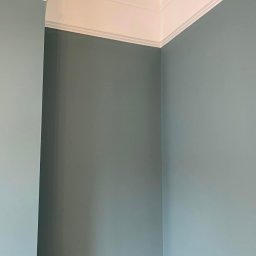 M&P Solid - Wnętrze pokoju po malowaniu ścian na odcień błękitu, z białym ozdobnym sztukaterią pod sufitem.