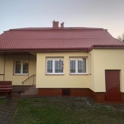 M&P Solid - Dom jednorodzinny z nową, czerwoną dachówką i świeżo pomalowaną elewacją w odcieniach beżu, widoczny z perspektywy trawnika z kostką brukową. W tle błękitny van.