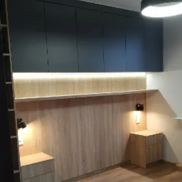 Ciemnoszare szafy na wymiar pod sufitem z oświetleniem LED nad drewnianym panelem ściennym i szafkami nocnymi w sypialni, oświetlenie sufitowe w kształcie pierścienia.