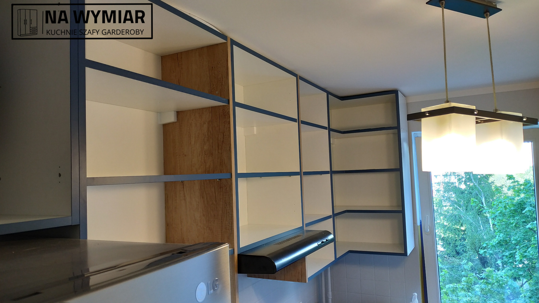 Biało-drewniana zabudowa kuchenna z niebieskimi akcentami w mieszkaniu w Warszawie, widok z dołu na górne szafki i okap.