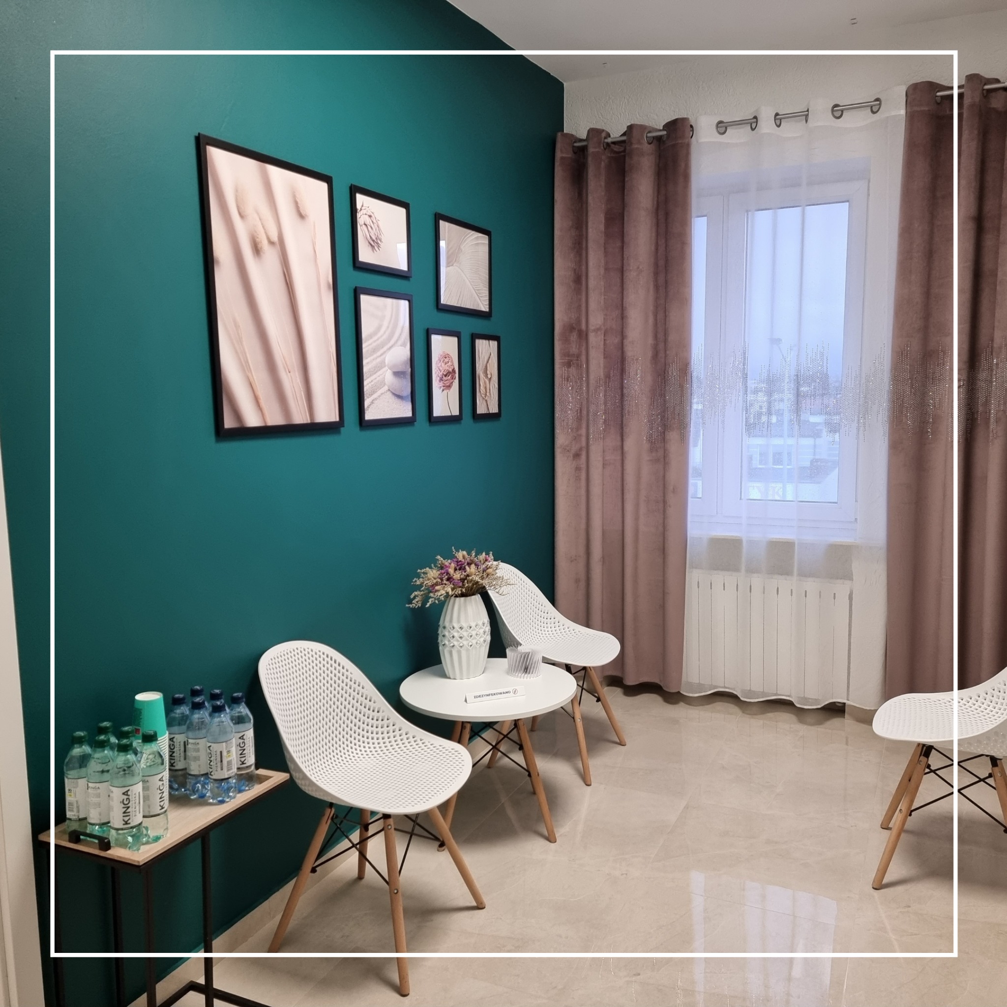 Poczekalnia: turkusowa ściana z ramkami, stolik z kwiatami, białe krzesła, woda mineralna na małym stoliku, okno z brązowymi zasłonami.
