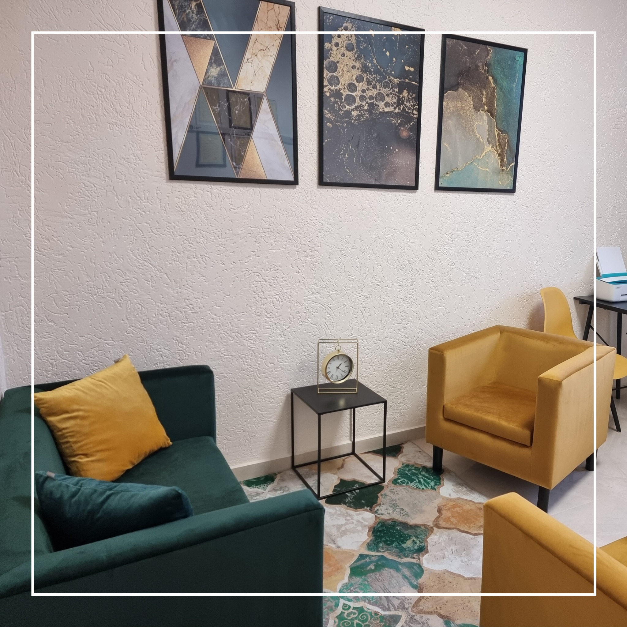 Wnętrze gabinetu z zieloną sofą z żółtą poduszką, żółtymi fotelami, stolikiem z zegarem i trzema obrazami na ścianie o fakturze baranka.