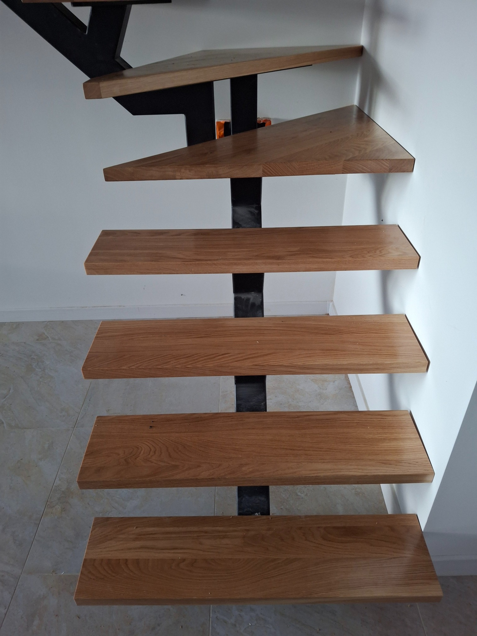 Schody z drewnianymi stopniami i czarną, metalową konstrukcją, widziane z dołu, pokazujące detale wykończenia i montażu przy ścianie.