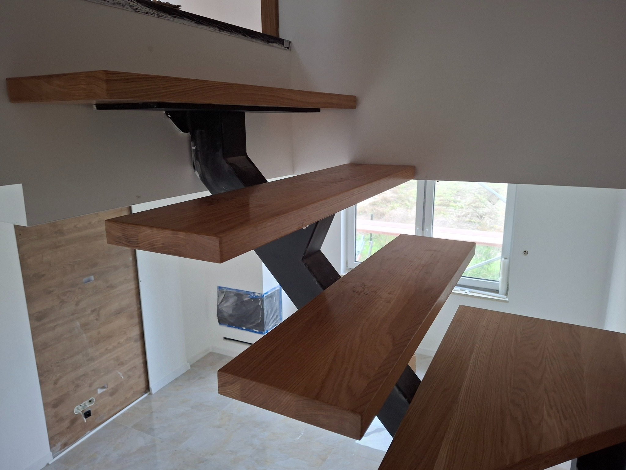 Nowoczesne schody z drewnianymi stopniami i metalową konstrukcją, widok z dołu, jasne wnętrze z oknem w tle, minimalistyczny design.