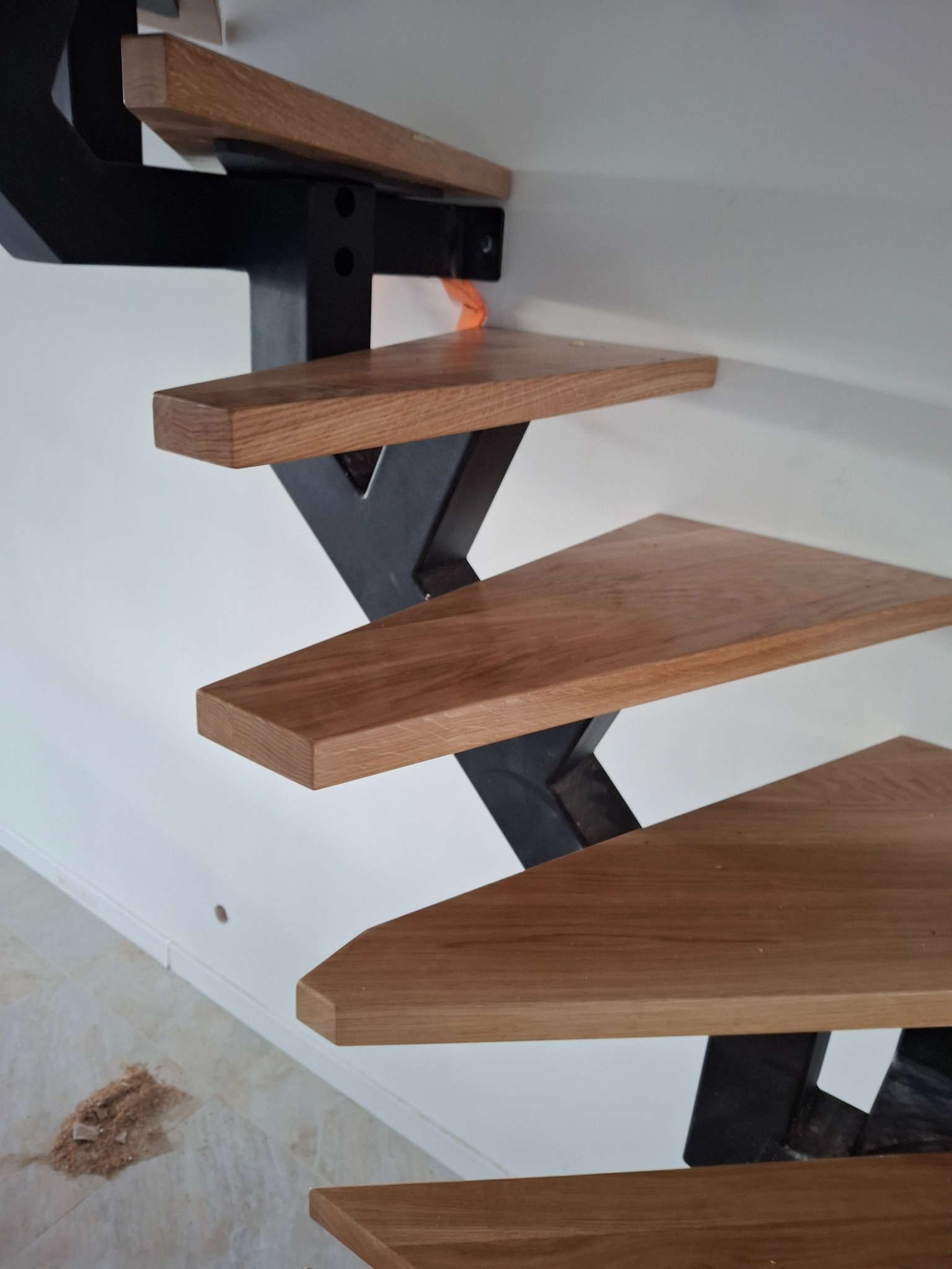 Nowoczesne schody: drewniane stopnie o ciepłym odcieniu na czarnej, metalowej konstrukcji, widok z dołu, minimalistyczny design, jasne tło ściany.