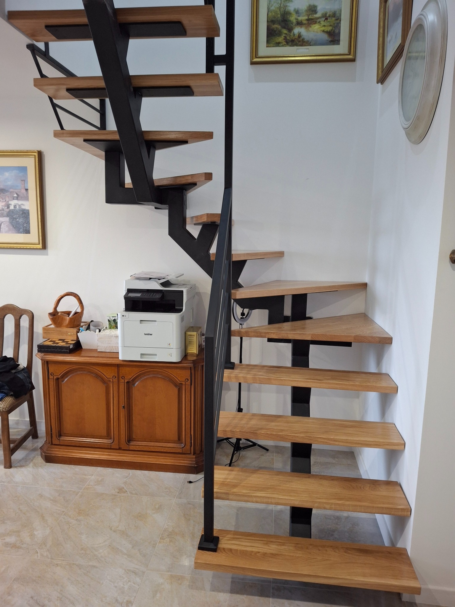 Nowoczesne schody z drewnianymi stopniami i czarną metalową konstrukcją, umieszczone w jasnym wnętrzu z elementami dekoracyjnymi na ścianach.