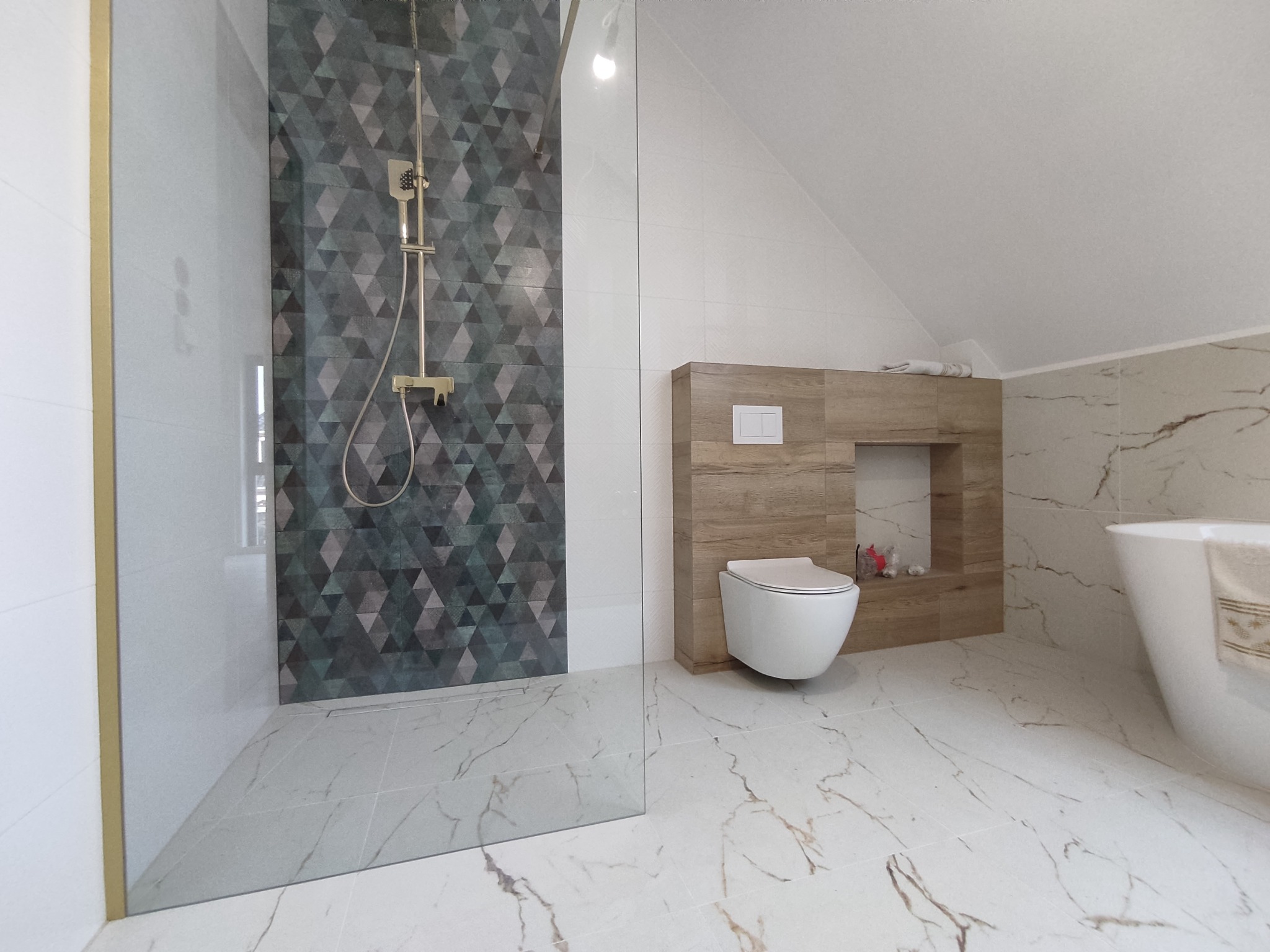 Nowoczesna łazienka na poddaszu z kabiną prysznicową typu walk-in, geometrycznymi płytkami na ścianie prysznica, wiszącą toaletą i marmurową podłogą.