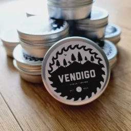 Stos metalowych puszek z etykietą 'Vendigo Żywica i Drewno' na drewnianym blacie, logo z motywem piły, drzew i jelenia.