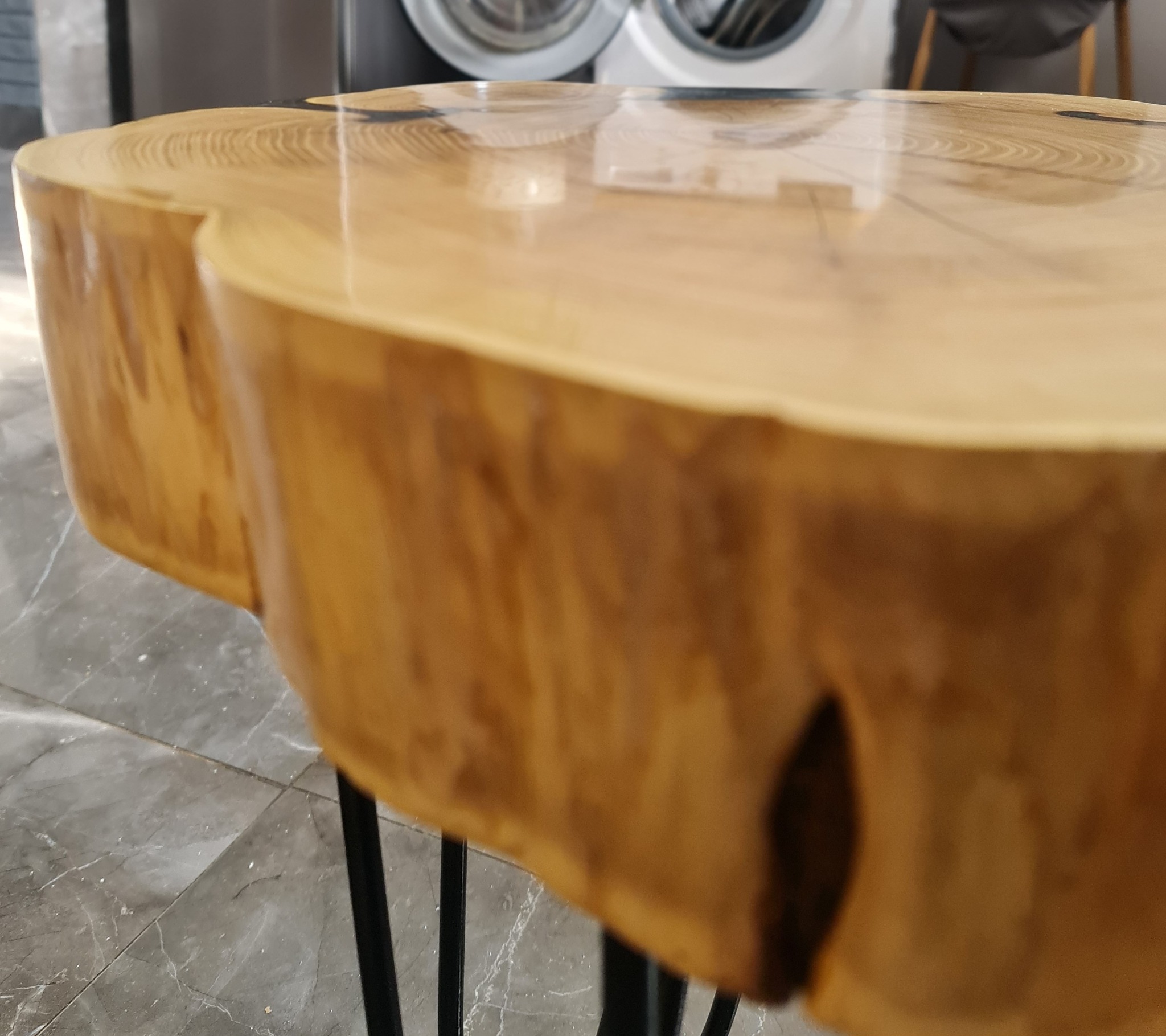 Stolik kawowy z blatem z plastra drewna, pokryty żywicą, na metalowych nóżkach typu hairpin, w tle pralka.