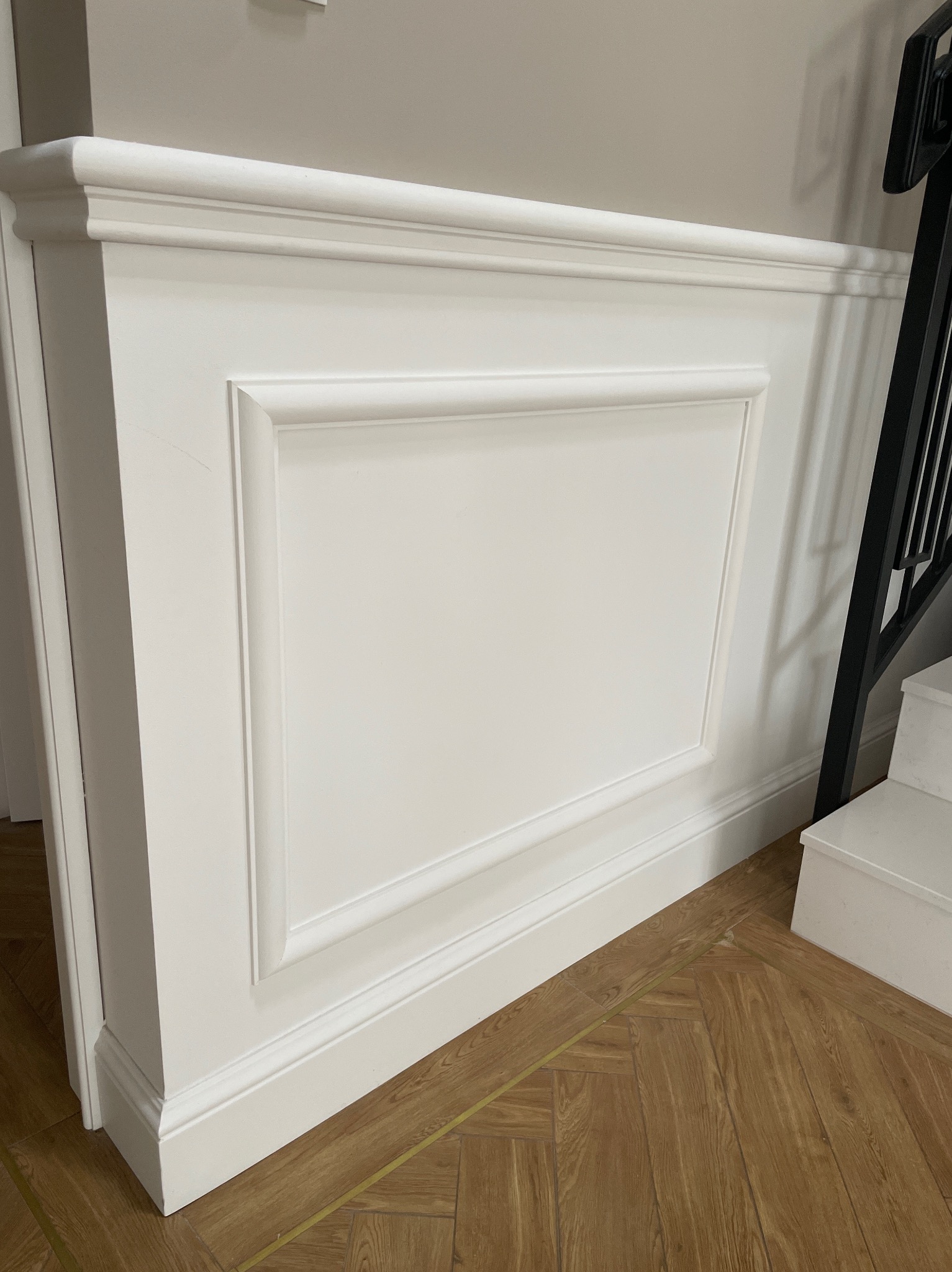 Biała sztukateria gipsowa z profilowanymi ramkami i listwami przypodłogowymi, montowana na ścianie przy schodach z parkietem ułożonym w jodełkę.