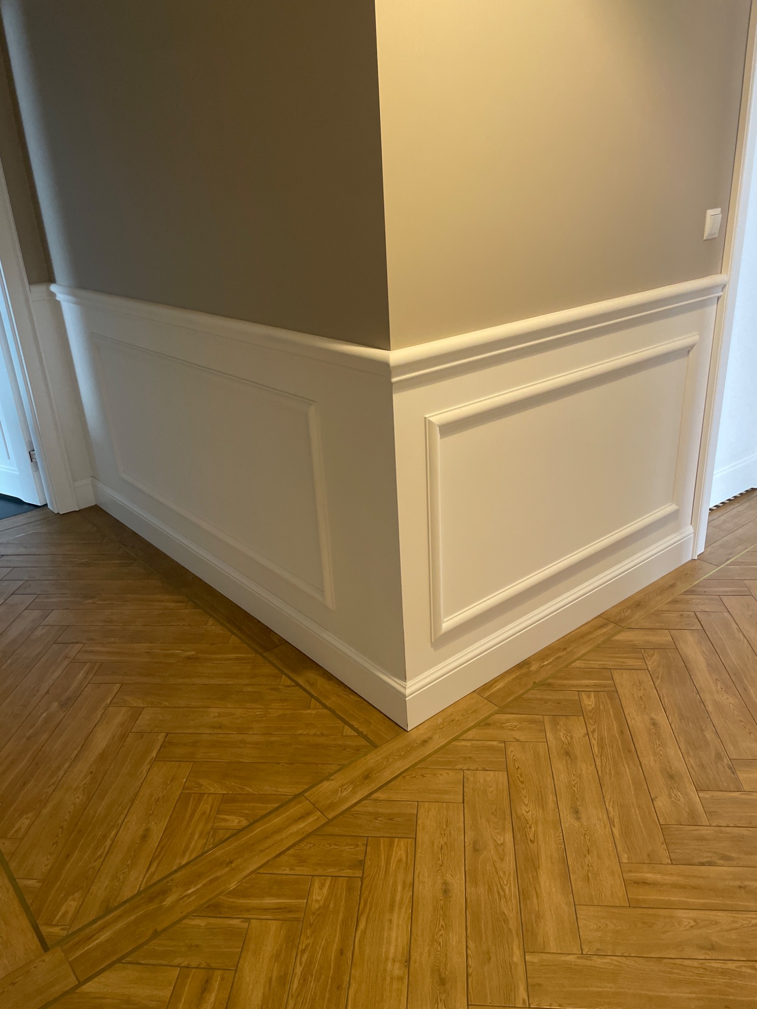 Eleganckie wykończenie narożnika pokoju z boazerią w stylu angielskim i parkietem ułożonym we wzór jodełki.