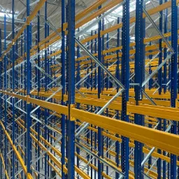 Puste, metalowe regały magazynowe w kolorze niebieskim i żółtym, widok z perspektywy, oświetlenie górne, hala magazynowa w tle.