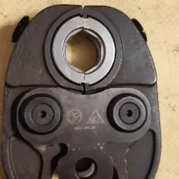 Zaciskarka do rur z widocznymi śrubami i oznaczeniami producenta na żółtym tle.