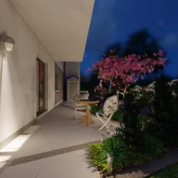 Wieczorny widok na taras z krzesłami i stolikiem, otoczony bujną roślinnością z kwitnącym drzewem na tle nocnego nieba.