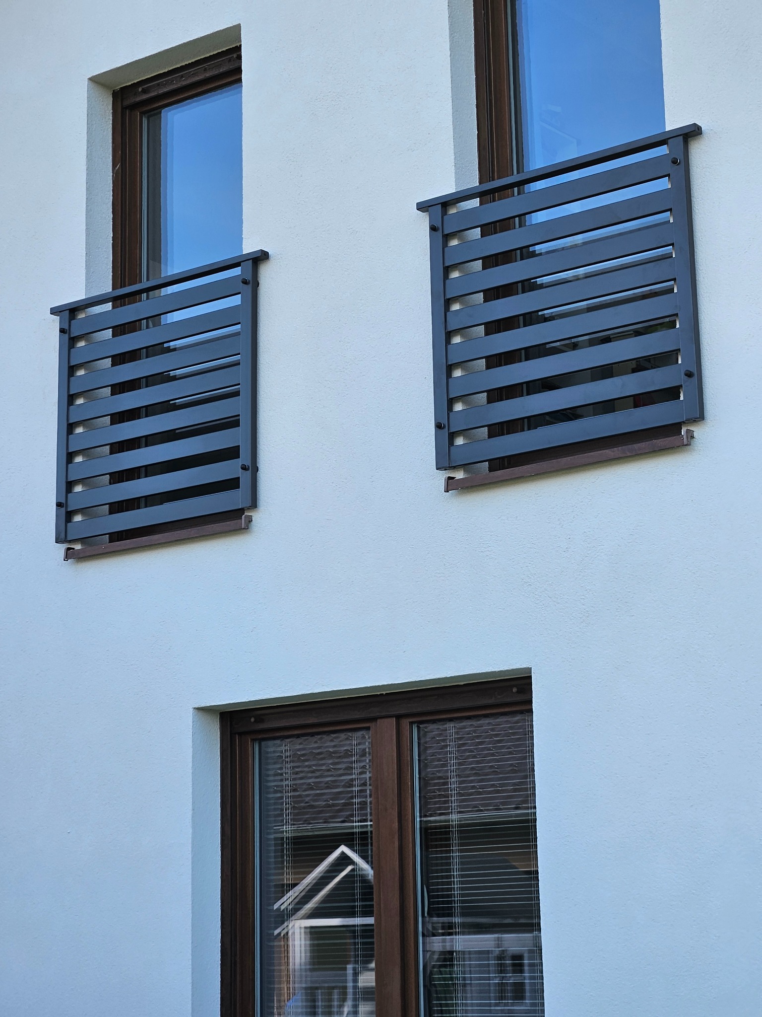 Elewacja budynku z oknami i nowoczesnymi, metalowymi zabezpieczeniami balkonowymi w kolorze grafitowym, zamocowanymi na zewnątrz.