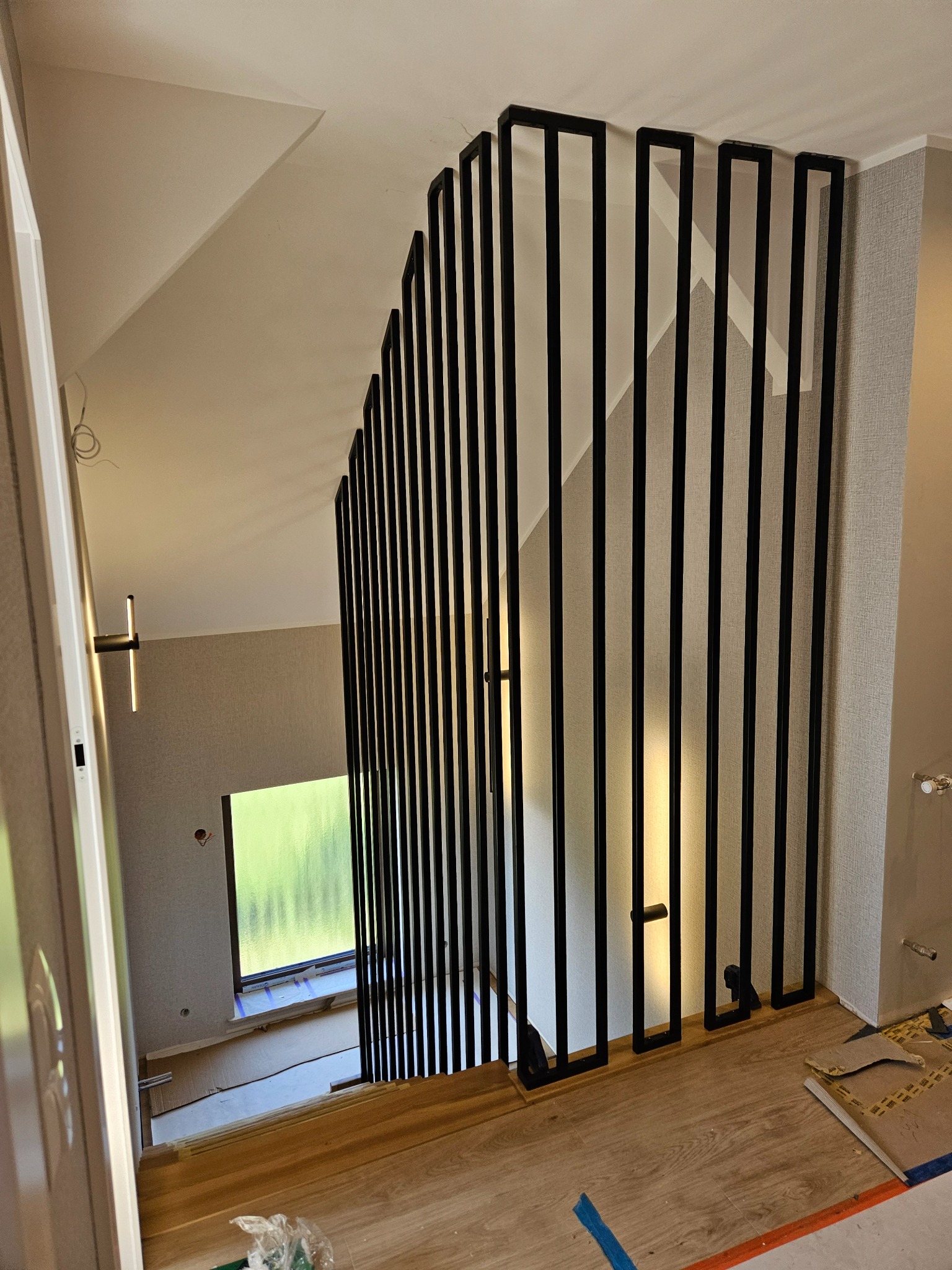 Nowoczesna, czarna balustrada schodowa z pionowych profili, widok z góry. Minimalistyczny design, jasne wnętrze, drewniane schody w trakcie wykończenia.