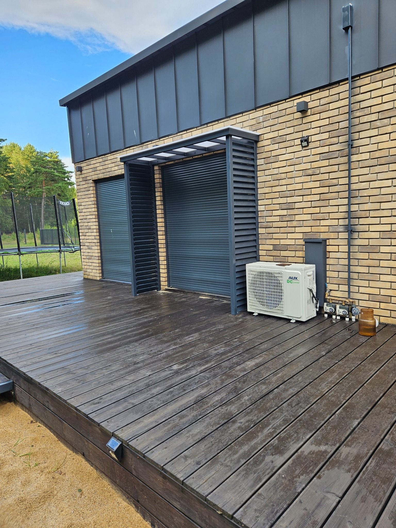 Zabudowa tarasu z roletami zewnętrznymi w Krzycku Wielkim, tworząca osłoniętą przestrzeń. Widoczna drewniana podłoga tarasu i klimatyzator na zewnątrz budynku.