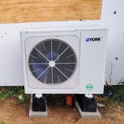 INNOVA Jakub Paszkowski - Biała pompa ciepła marki York, model z czynnikiem chłodniczym R32, umieszczona na betonowych podstawach przy ścianie budynku z fakturą baranka i drewnianym wykończeniem.