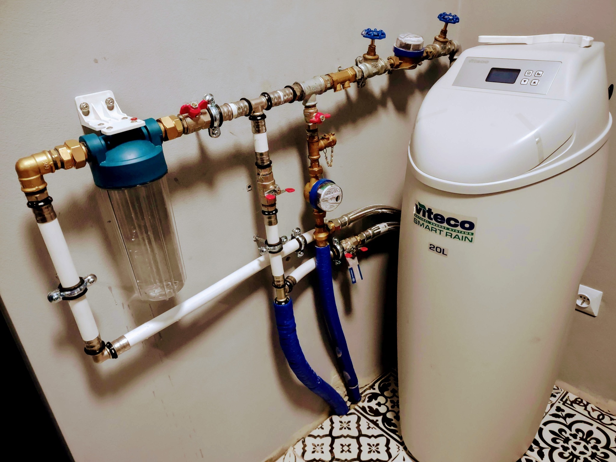 System uzdatniania wody Viteco Smart Rain 20L z filtrem wstępnym, zaworami i rurami zamontowany na ścianie nad ozdobną podłogą.