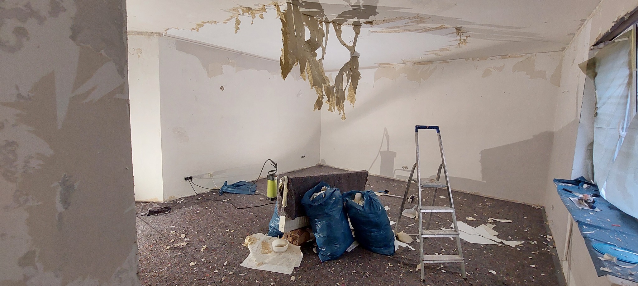 Pokój w trakcie usuwania starej tapety z sufitu i ścian, widoczne worki na śmieci, drabina i resztki tapety na podłodze.