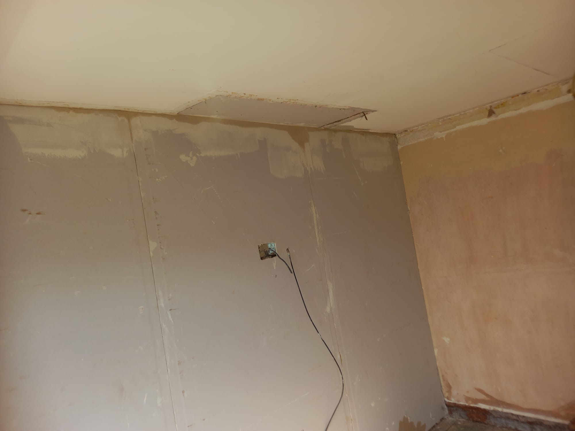 Niedokończone szpachlowanie ścian w rogu pokoju, widoczne ślady po naprawie sufitu i wystająca instalacja elektryczna.