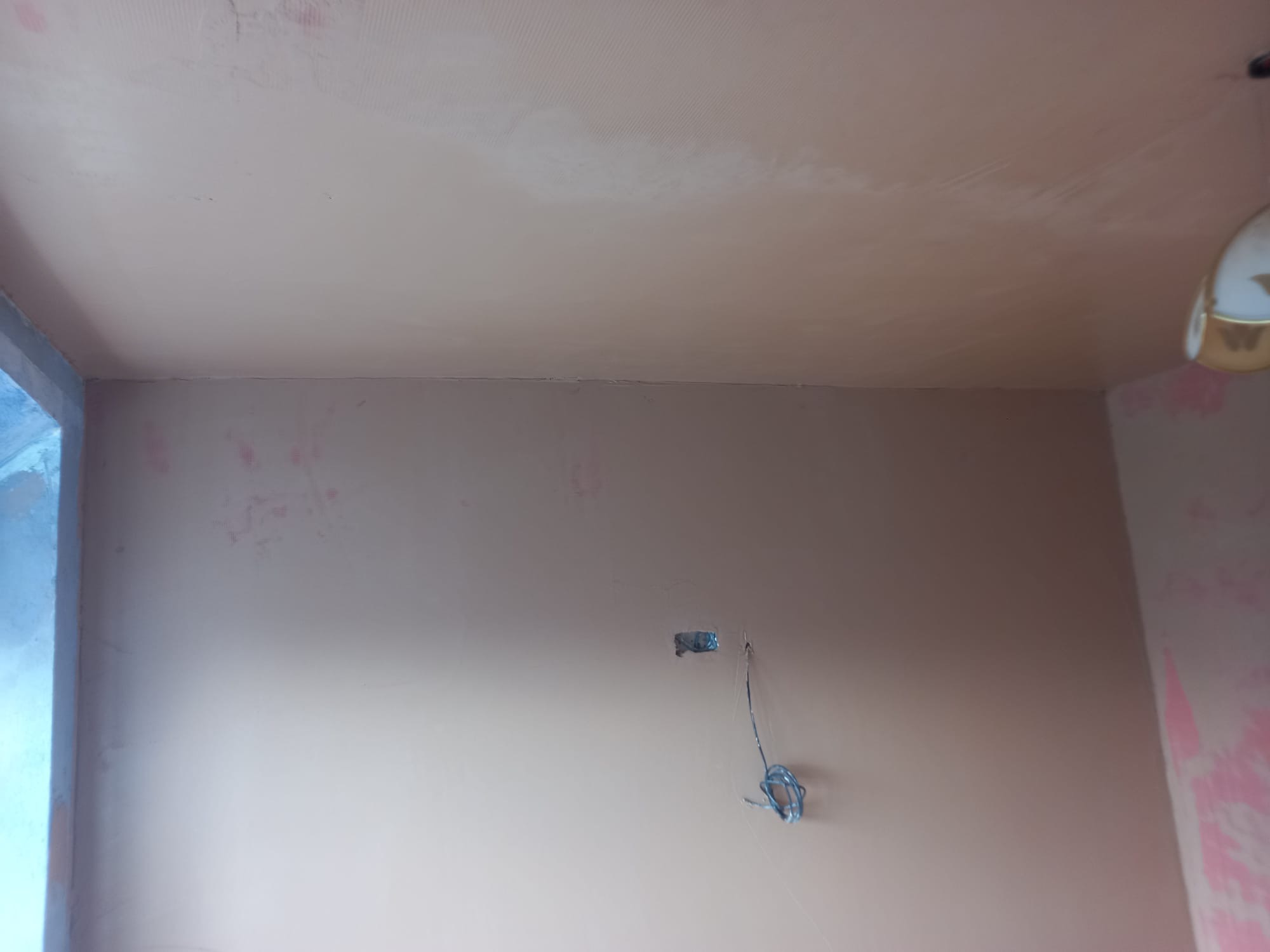 Świeżo wyszpachlowany sufit i ściana z widocznymi śladami po taśmie zbrojącej oraz wystającymi przewodami elektrycznymi ze ściany.